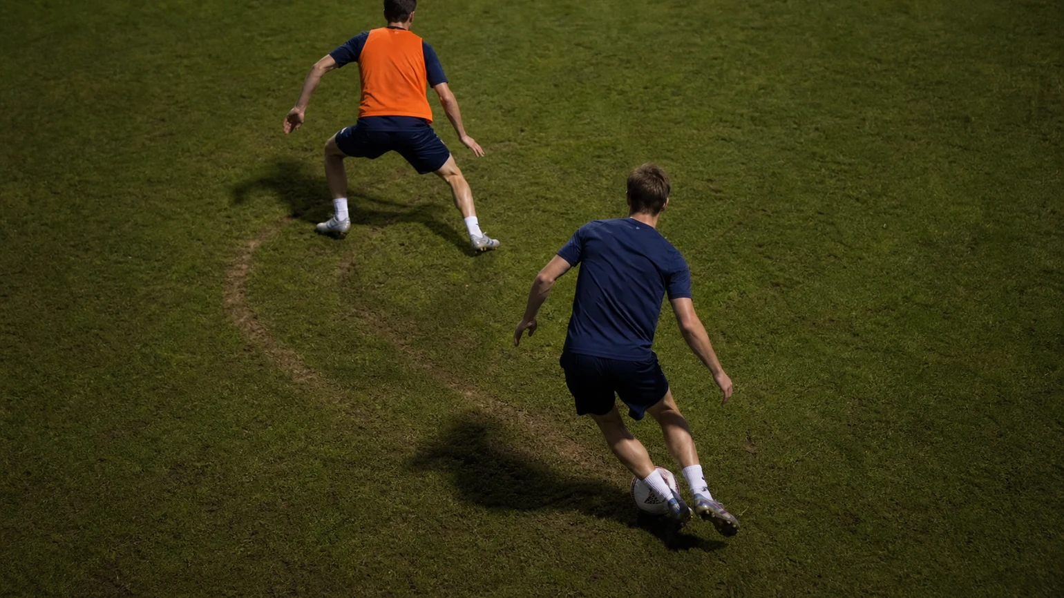 an attacker checking away from a marker then spinning back into space, the double-move path worn into the grass